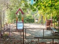 Small empty playground in the yard. A small children's fenced playground on sandy ground strewn with dry foliage, in Royalty Free Stock Photo