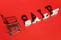 Small empty shopping trolley cart and word SALE of white letters casts a large shadow on red background with copy space. Concept Royalty Free Stock Photo