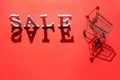 Small empty shopping trolley cart and word SALE of white letters casts a large shadow on red background with copy space. Concept Royalty Free Stock Photo