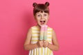 Small European kid biting fruit ice cream, little charming girl with widely opened mouth, wearing summer clothes, looks happy, Royalty Free Stock Photo