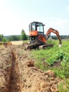 Small excavator of Hitachi and narrow trench for cable in ground at rural area in summer