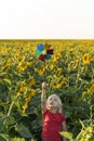 Small, fair-haired boy stands among field of sunflowers and raised windmill toy high above his head