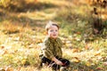 A small fair-haired cute boy in a checkered yellow shirt is sitting on a lawn