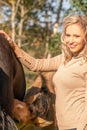 Small falcon color foal drinks some milk from its mother. Young smiling woman is standing next to the foal. Close-up Royalty Free Stock Photo