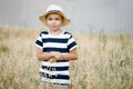 Small farm boy, smiling and looking at the camera, stands in an oat field. Cute boy in a straw hat and a striped T-shirt Royalty Free Stock Photo