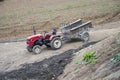 Small farm red tractor with empty trailer in the field in the end of the growing season in autumn Royalty Free Stock Photo