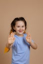 Small fascinated Caucasian girl having kanekalon braids showing hands palms playing smiling with missing tooth looking