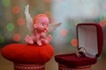 A small figure of an angel sitting on or near a jewelry box close up, a background bokeh of twinkling party lights