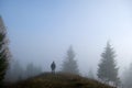 Small figure of lonely hiker enjoying his time on wild forest trail on foggy autumn day