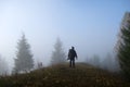 Small figure of lonely hiker enjoying his time on wild forest trail on foggy autumn day