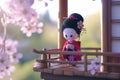 A small figurine of a geisha doll stands against a blurred traditional Japanese background, evoking the elegance and Royalty Free Stock Photo