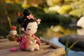 A small figurine of a geisha doll stands against a blurred traditional Japanese background, evoking the elegance and Royalty Free Stock Photo