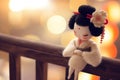 A small figurine of a geisha doll stands against a blurred traditional Japanese background, evoking the elegance and Royalty Free Stock Photo