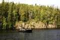 A small fishing boat against the rocky wooded shore of the island of Valaam.