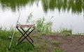 A small fishing chair for one person with a military print stands on the grass next to the lake. Fishing concept. Royalty Free Stock Photo