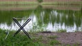 A small fishing chair for one person stands on the grass next to the lake. Fishing concept. Royalty Free Stock Photo