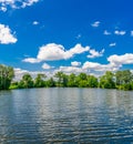 Small flat lake against the sky with clouds. Trees on the shore of the reservoir. Summer holidays, fishing