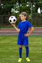 A small football player with a ball stands on a green football field