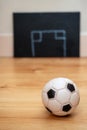 Small football on a wooden floor in focus. Abstract goal post drawn on a black board out of focus in the background. Soccer tactic Royalty Free Stock Photo