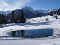 Small frozen water pond surrounded on a snowy day with the Hochalm Mountain in the background