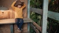 Small, funny child in big cowboy hat is sitting on wooden porch of country house Royalty Free Stock Photo