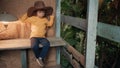Small, funny child in big cowboy hat is sitting on wooden porch of country house Royalty Free Stock Photo