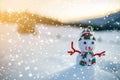 Small funny toy baby snowman in knitted hat and scarf in deep snow outdoor on blurred mountains landscape and falling big Royalty Free Stock Photo