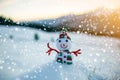 Small funny toy baby snowman in knitted hat and scarf in deep snow outdoor on blurred mountains landscape and falling big Royalty Free Stock Photo