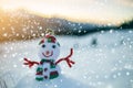 Small funny toy baby snowman in knitted hat and scarf in deep snow outdoor on blurred mountains landscape and falling big Royalty Free Stock Photo