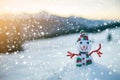 Small funny toy baby snowman in knitted hat and scarf in deep snow outdoor on blurred mountains landscape and falling big Royalty Free Stock Photo