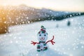 Small funny toy baby snowman in knitted hat and scarf in deep snow outdoor on blurred mountains landscape and falling big Royalty Free Stock Photo