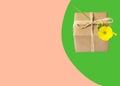Small gift box wrapped in brown paper tied with twine yellow flower on on duotone pink green background. Present for mothers day