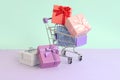 Small gift boxes of different colors with ribbons lies in shopping cart on a violet and blue pastel background Royalty Free Stock Photo