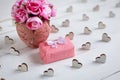 Small gift wrapped in paper with wooden hearts around and pink flowers in vase on white wooden background Royalty Free Stock Photo