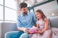 Small girl adn her dad holding gift box sitting on the couch at home