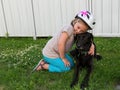 Small girl with bicycle helmet kneeling in grass holding black labrador Royalty Free Stock Photo