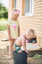 Small girl with blond curly hair and ittle boy play in the yard of the house in the sand. Royalty Free Stock Photo