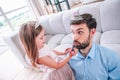 Small girl in dress applying lipstick on dad lips, having fun together at home Royalty Free Stock Photo