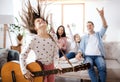 Small girl with family indoors at home, having fun with guitar.