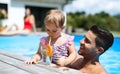 Small girl with father drinking lemonade in swimming pool outdoors in backyard garden.