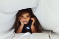 a small girl with a flashlight reading a book in bed Royalty Free Stock Photo