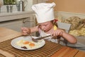 Small girl has a snack. Little girl eats ham and eggs. Cute girl wears chef costume. Family and childhood concept.