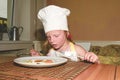 Small girl has a snack. Little girl eats ham and eggs. Cute girl wears white chef costume. Family and childhood concep