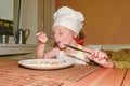 Small girl has a snack. Little girl eats ham and eggs. Cute girl wears white chef costume. Family and childhood concep