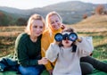 Small girl with mother and grandmother on a walk in autumn nature, using binoculars. Royalty Free Stock Photo