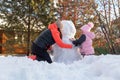 Small girl with mother sitting on snow making snowman with hands on backyard in evening with rowan and fir trees in Royalty Free Stock Photo