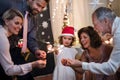 Small girl with parents and grandparents indoors celebrating Christmas, holding sparklers.