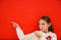 Small girl pointing away at copy space with two fingers isolated over red background