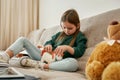 The small girl putting coins into a unicorn moneybox while sitting alone on the sofa in a well lighted room, fully