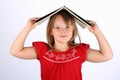 Small girl in red holding a book on her head Royalty Free Stock Photo